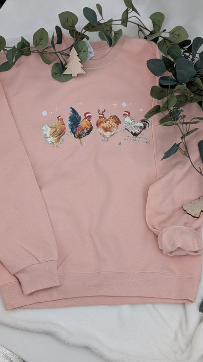 Pink sweatshirt with embroidered designs on a white surface with greenery.