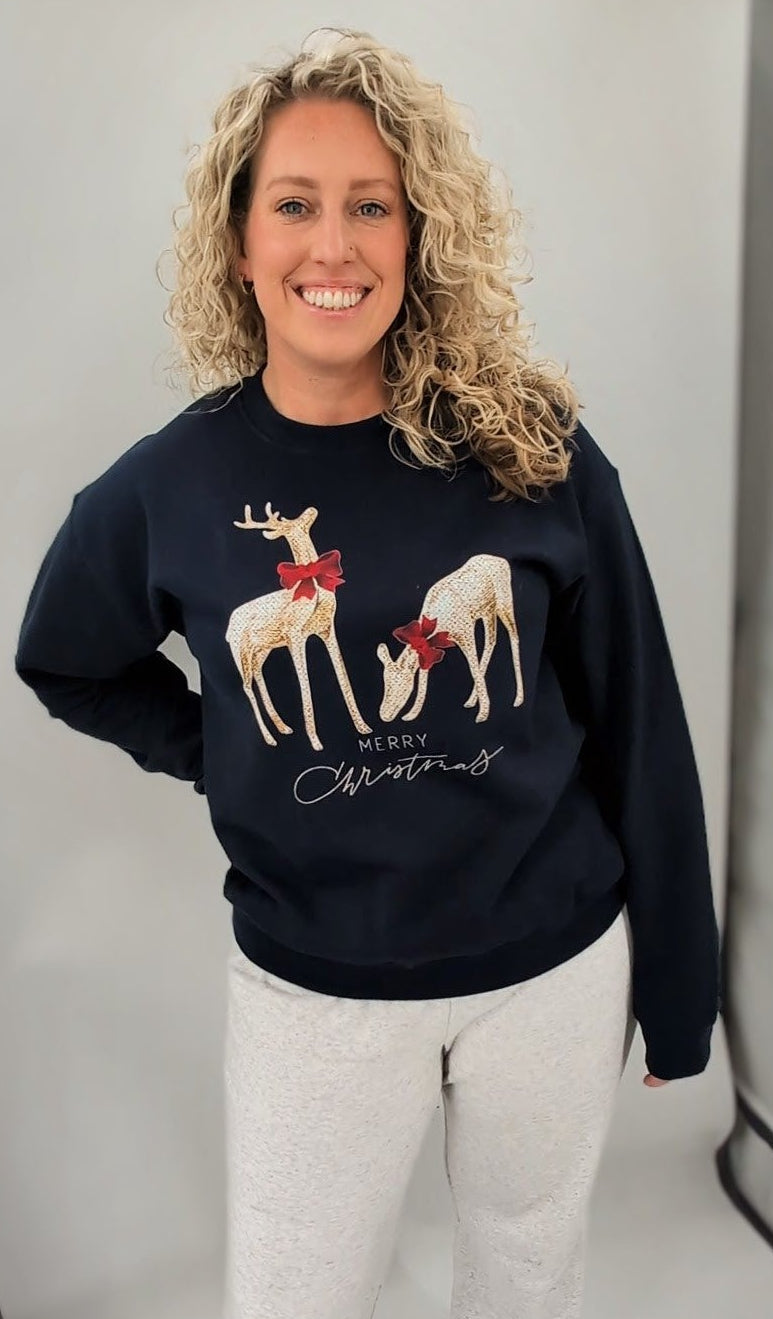 Woman wearing a navy blue sweater with reindeer graphics in a photo studio setting.